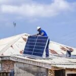 A young Nigerian solar technician installing rooftop panels under bright sunlight in Abuja. Image Description