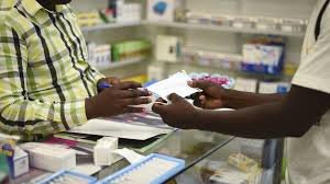 A Nigerian pharmacist examining medicine packs behind a pharmacy counter