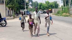 Out-of-school children sitting along a street in Northern Nigeria, highlighting the country’s education crisis.