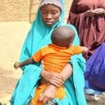 Teenage mother holding child in Kano community