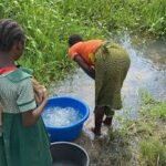 A Nigerian woman standing beside a rural riverbank where communities depend on untreated water amid growing concerns over schistosomiasis infections.