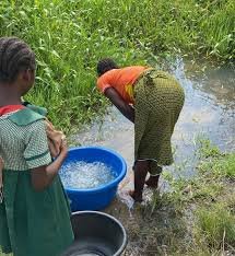 A Nigerian woman standing beside a rural riverbank where communities depend on untreated water amid growing concerns over schistosomiasis infections.